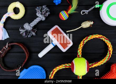 Verschiedene Accessoires für Hunde und Katzen: Mausspielzeug, Ball, Kamm, Leine, Kragen, Spielzeug und Schüssel mit Knochen auf schwarzem Holzhintergrund. Haustiere Pflege und Rout Stockfoto