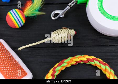 Verschiedene Accessoires für Hunde und Katzen: Mausspielzeug, Ball, Kamm, Leine, Kragen, Spielzeug und Schüssel mit Knochen auf schwarzem Holzhintergrund. Haustiere Pflege und Rout Stockfoto