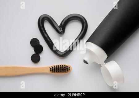 Herz aus schwarzer Zahnpasta, Aktivkohle-Pillen, Pinsel und Tube auf hellem Hintergrund Stockfoto