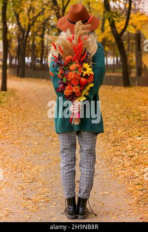 Junge Frau hält im Herbstpark einen Strauß hinter ihrem Rücken Stockfoto