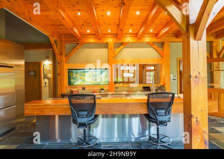 Insel mit Edelstahl-Arbeitsplatte und geölten Kiefernholz Bar mit schwarzem Kunststoff und Leder hohe Rückenstühle in der Küche im Holzrahmen Haus Stockfoto