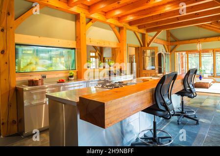 Insel mit Edelstahl-Arbeitsplatte und geölten Kiefernholz Bar mit schwarzem Kunststoff und Leder hohe Rückenstühle in der Küche im Holzrahmen Haus Stockfoto