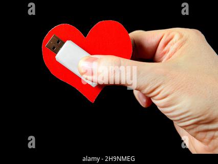 Herzform und USB-Laufwerk in der Hand auf dem schwarzen Hintergrund Stockfoto