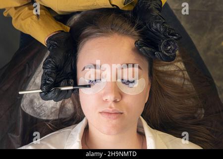 Ein Mädchen in einem Schönheitssalon auf dem Verfahren der Färbung ihrer Wimpern. Pflege für Augenbrauen und Wimpern. Der Make-up-Meister malt die Wimpern des Kunden. Stockfoto