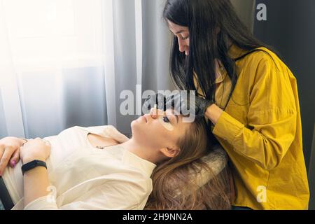 Ein Mädchen in einem Schönheitssalon auf dem Verfahren der Färbung ihrer Wimpern. Pflege für Augenbrauen und Wimpern. Der Make-up-Meister malt die Wimpern des Kunden. Stockfoto