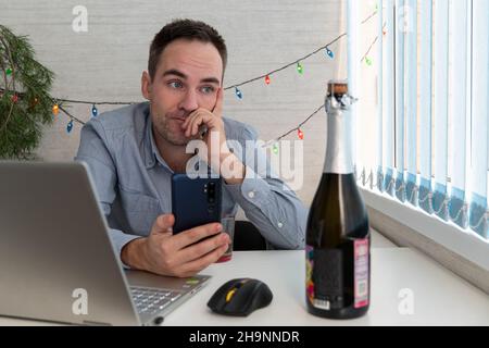 Junger Geschäftsmann trinkt aus Stress. Alkoholismus am Arbeitsplatz. Ein müder oder kranker Mitarbeiter schaut auf eine Flasche Champagner, will New y feiern Stockfoto