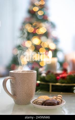 Eine Tasse Heißgetränk und im Hintergrund verschwommene Kerzen und ein Weihnachtsbaum Stockfoto