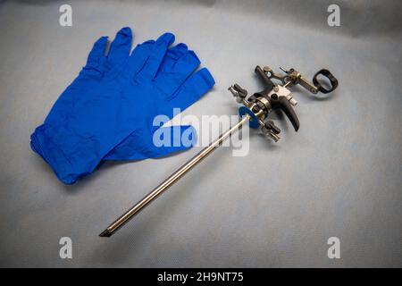 Ein Instrument zur Durchführung einer Prostataresektion liegt neben blauen medizinischen Handschuhen und einer Glasspritze Stockfoto