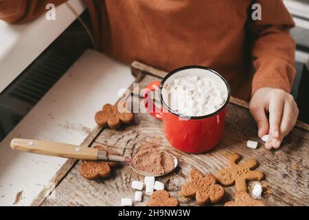 Kinder trinken Kakao mit Salmler und weihnachtslebkuchenmann auf einem hölzernen Hintergrund. Weihnachtsbonbons mit Kakao und Marschmalereien für Kinder Stockfoto