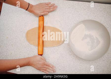 Der Konditor rollt den Teig mit Nudelholz aus und macht leckere Ingwer-Kekse. Kochen und Dekorieren weihnachtsdessert. Stockfoto