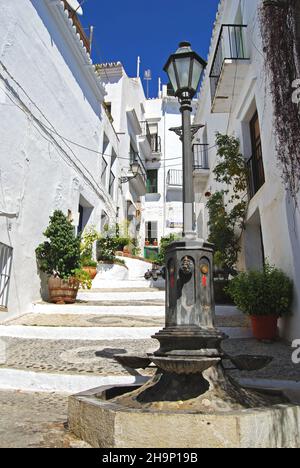 Blick entlang einer typischen steilen Dorfstraße mit Licht im Vordergrund/Trinkbrunnen im Vordergrund, Frigiliana, Spanien. Stockfoto