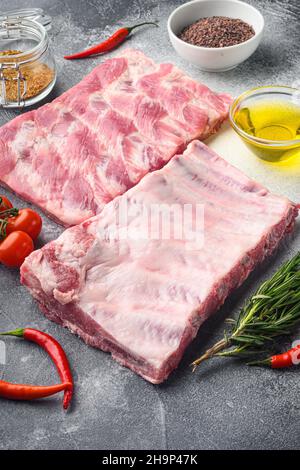 Frisches Rack aus rohen Schweinefleisch-Spare-Rippen gewürzt mit Gewürzen-Set, auf grauem Hintergrund Stockfoto