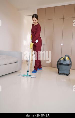 Fokussierter professioneller junger Reiniger, der das Wohnzimmer wischt Stockfoto