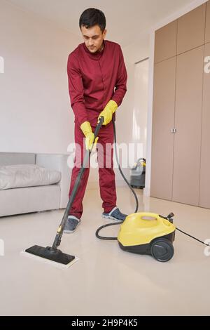 Konzentrierter Hausierer in Gummihandschuhen mit Dampfreinigungsgerät Stockfoto