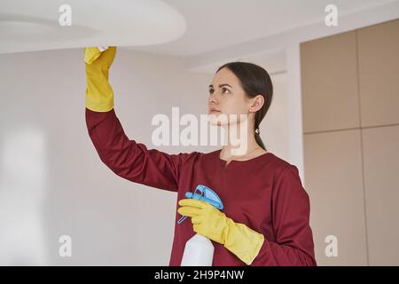 Fokussierter Hausierer in Gummihandschuhen zur Reinigung der Deckenhalterung Stockfoto