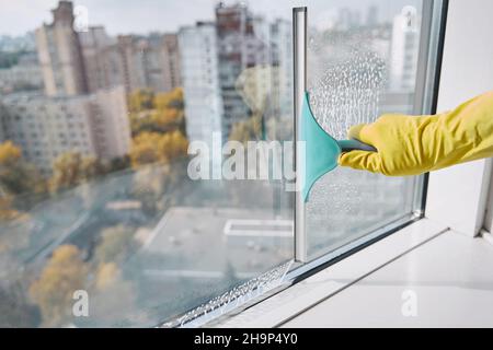 Fensterscheibe mit Handschuhen und Arbeitsgerät mit Gummiklinge Stockfoto