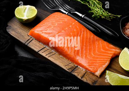 Lachs. Set aus frischem, rohem Lachsfisch-Filet mit Kräutern auf schwarzem Hintergrund mit dunklem Stein Stockfoto