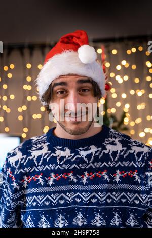 Porträt eines lächelnden jungen Mannes mit rotem Hut vor einer Wand aus Weihnachtslichtern - Konzept des Glücks während der Weihnachtszeit Stockfoto