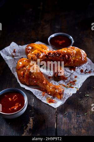 Ein großer Winkel von appetitlich gebratenen Hähnchendrumsticks, serviert mit würziger Sauce, auf einem Holztisch im Restaurant Stockfoto