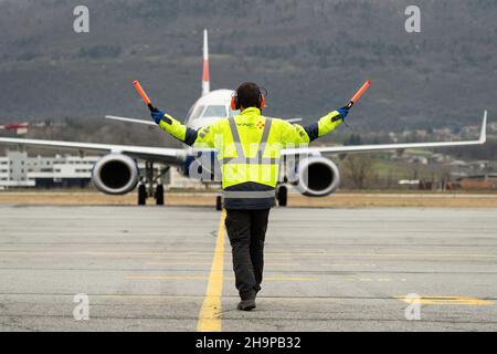 Mitglied der Bodencrew von Vinci Airports, die Kommandos zu einem Flugzeug auf dem Asphalt gibt Stockfoto