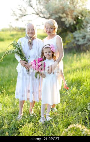 Europäische glückliche Großmutter in weißem Kleid mit Tochter und Enkelin draußen. Stockfoto