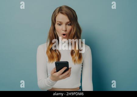 Schockiert Millennial Mädchen schaut auf Handy mit überrascht Gesicht, Augen poppte und Mund weit geöffnet Stockfoto