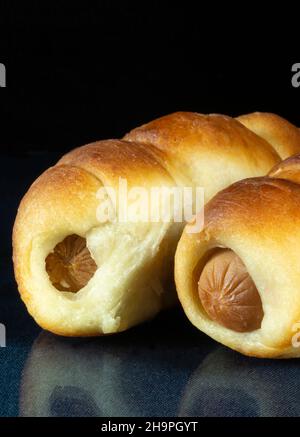 Der Hot Dog im Test auf schwarzem Hintergrund mit Reflexion auf dem Tisch. Leckeres Backen am Abendessen. Produkte der Fütterung Stockfoto