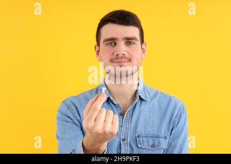 Junger Mann hält Hörgeräte auf gelbem Hintergrund Stockfoto