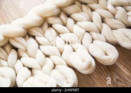 Der Prozess des Strickens eines Plaid großen Strick aus Merinowolle. Unvollendete Arbeit mit offenen Schlaufen auf Holzboden Stockfoto