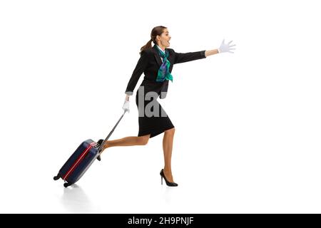 Ganzkörperportrait einer schönen jungen Frau, Flugbegleiterin, die mit einem Koffer auf weißem Studiohintergrund läuft. Stockfoto