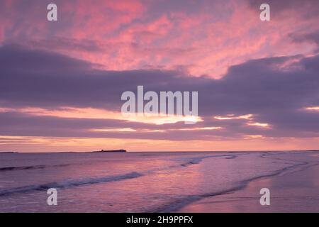 Die Morgendämmerung bricht über Bamburgh Beach und den Farne Islands, Northumberland, England. Stockfoto