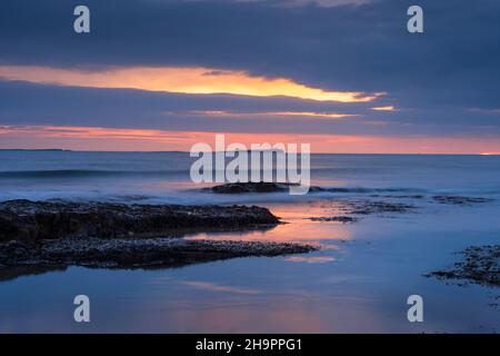 Die Morgendämmerung bricht über Bamburgh Beach und den Farne Islands, Northumberland, England. Stockfoto