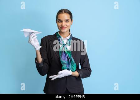 Halblanges Porträt eines schönen jungen Mädchens, Flugbegleiter in schwarzer Uniform posiert isoliert auf blauem Studiohintergrund. Stockfoto