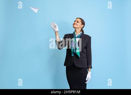 Halblanges Porträt eines schönen jungen Mädchens, Flugbegleiter in schwarzer Uniform posiert isoliert auf blauem Studiohintergrund. Stockfoto