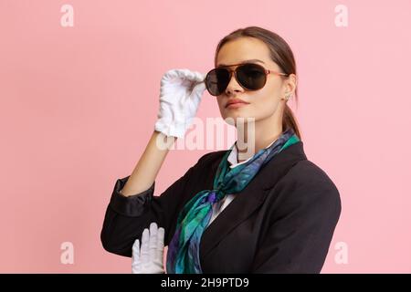 Stilvolle junge Mädchen, weibliche Flugbegleiterin trägt eine Sonnenbrille Blick auf die Kamera isoliert auf rosa Studio Hintergrund. Stockfoto