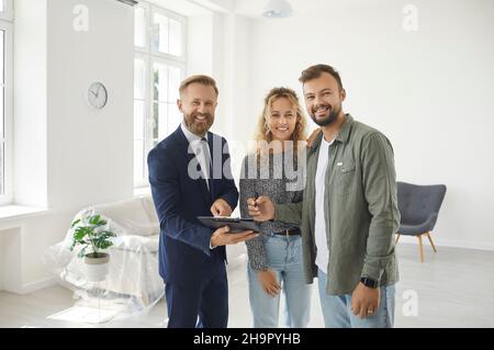 Porträt eines glücklichen jungen Paares, das während eines Treffens mit einem Immobilienmakler einen Vertrag unterzeichnet. Stockfoto