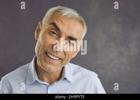 Nahaufnahme eines glücklichen älteren Mannes, der fröhlich an der Kamera zuzwinkert und ein Schild mit gutem Angebot zeigt. Stockfoto