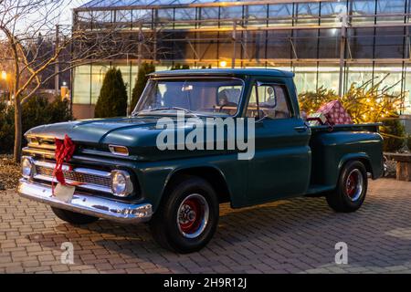 Green Vintage Pickup Truck dekoriert mit einem roten Bogen und Geschenkpakete und Lichter hinten für Weihnachten in der Dämmerung Stockfoto