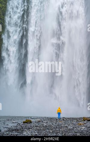 Riesiger Wasserfall hinter einer Person, Skogafoss Wasserfall, Südisland, Island Stockfoto