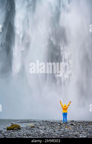 Riesiger Wasserfall hinter einer Person, Skogafoss Wasserfall, Südisland, Island Stockfoto