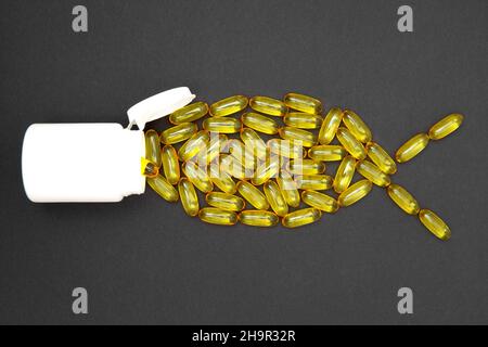 Omega-3 Fischöl-Softgels, die in einer Fischform angeordnet sind und in einer weißen Apothekenflasche auf schwarzem Hintergrund schwimmen. Stockfoto