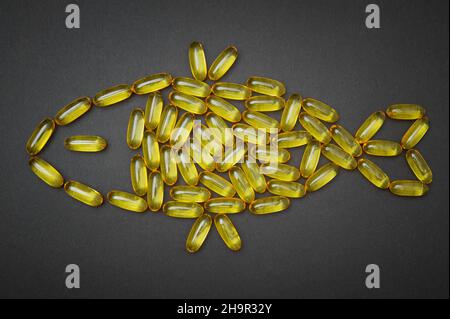 Omega-3 Fischöl-Softgels, die in einem Fischsymbol auf schwarzem Hintergrund angeordnet sind. Fettsäuren Nahrungsergänzungsmittel. Stockfoto