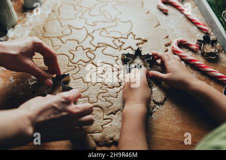 Frohe Weihnachten, Frohes neues Jahr. Lebkuchen kochen, backen. Mama und Tochter machen Kekse, schneiden verschiedene Formen von Cookies mit Metallform auf Holztisch in der Küche. Hochwertige Fotos Stockfoto