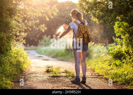 Die Frau wendet während der Wanderung in der Natur Insektenschutzmittel gegen Moskito und Zecke auf ihre Hand an. Hautschutz gegen Insektenstich Stockfoto