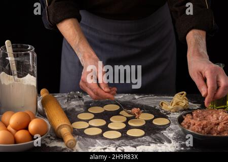 Ein Mann legt Hackfleisch auf die zubereiteten runden Teigformen, den Prozess der Herstellung eines traditionellen russischen Teigknödel Stockfoto