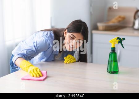 Fröhliche junge Frau, die den Esstisch in der Küche putzt Stockfoto