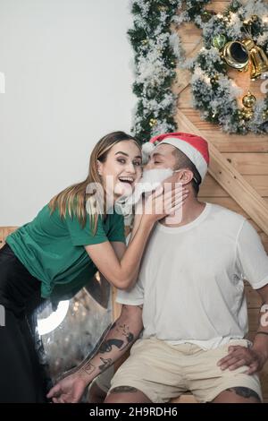 Porträt von schönen Paar. Neujahrsfoto des glücklichen Paares. Lachen und Spaß zusammen haben. Mann in rotem Weihnachtshut und Kunstbart Stockfoto