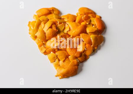 Defokussieren Sie den orangefarbenen herzförmigen Weihnachtshintergrund aus den Schalen von Orange und Mandarine auf einem weißen Hintergrund. Viele kleine Stücke getrockneter Schale. Liebe w Stockfoto