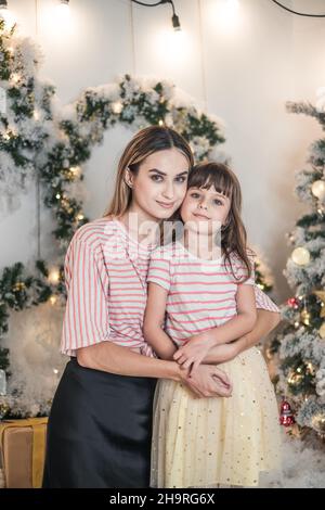 Weihnachts-Studio-Familiendreh. Neujahrsfoto der glücklichen Familie. Schöne Mutter und nette Tochter umarmen einander und lächeln Stockfoto