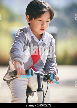 Fünf Jahre alter asiatischer kleiner Junge, der im Freien Fahrrad fährt Stockfoto